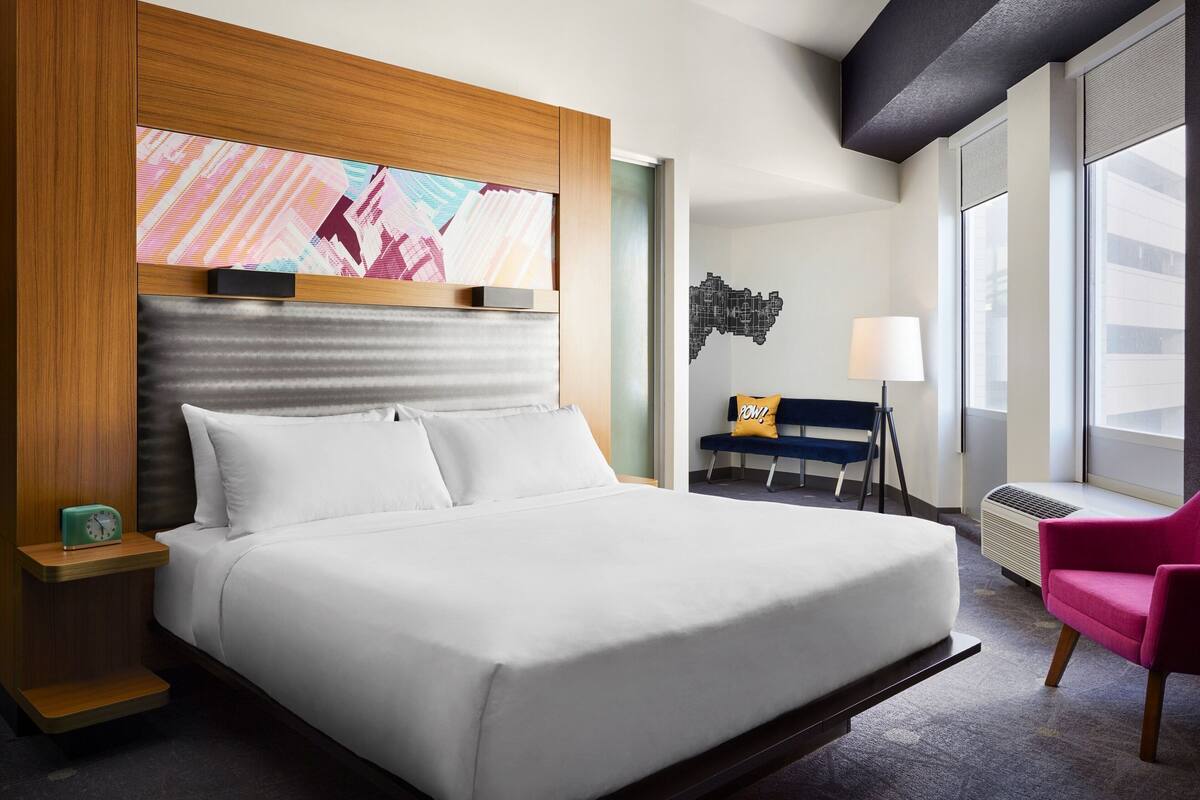 Ein Hotelzimmer mit einem großen Bett, einem Schreibtisch, einem Sessel, einer Lampe und einem Fenster.
