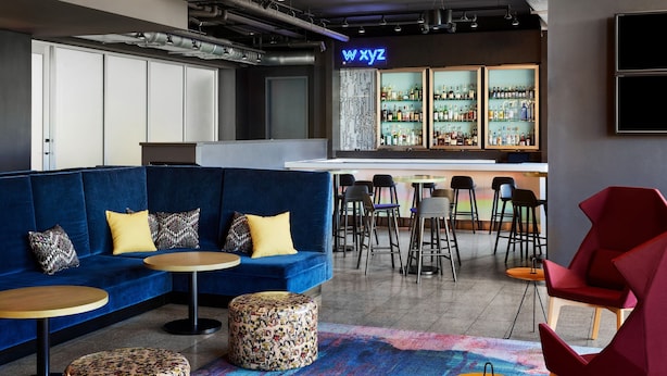 Zona de bar moderna con sofá azul, mesas redondas y una barra con estantes llenos de botellas.