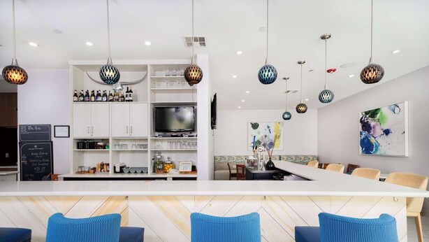 A modern kitchen with a central island, bar seating, and hanging pendant lights. - Hilton Garden Inn Houston/Clear Lake NASA (Webster)