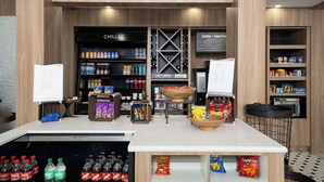 A coffee shop interior with a counter displaying snacks and beverages, shelves stocked with coffee and snacks, and a sign indicating 'The Shop' above the entrance. - Hilton Garden Inn Houston/Clear Lake NASA (Webster)