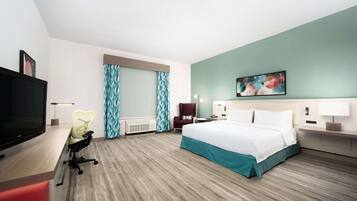A hotel room with a bed, a desk with a computer, a chair, a TV, and a painting on the wall.