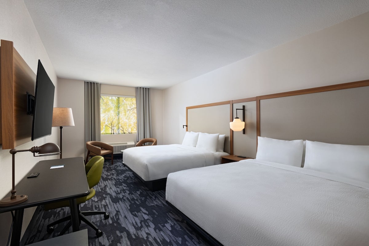 A hotel room with two beds, a desk with a chair, a TV, and a window with curtains.
