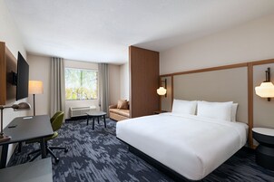 Habitación de hotel con una cama grande, un escritorio, una silla, una mesita, un televisor y una ventana con cortinas.