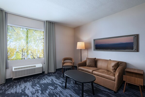 Une chambre d’hôtel avec une grande fenêtre, un canapé en cuir marron, une petite table, une lampe et un tableau au mur.