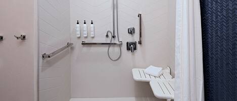 A modern bathroom with a shower, toilet, and handrails.