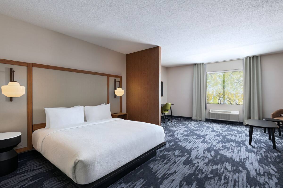 A hotel room with a large bed, a desk, a chair, and a window with curtains.