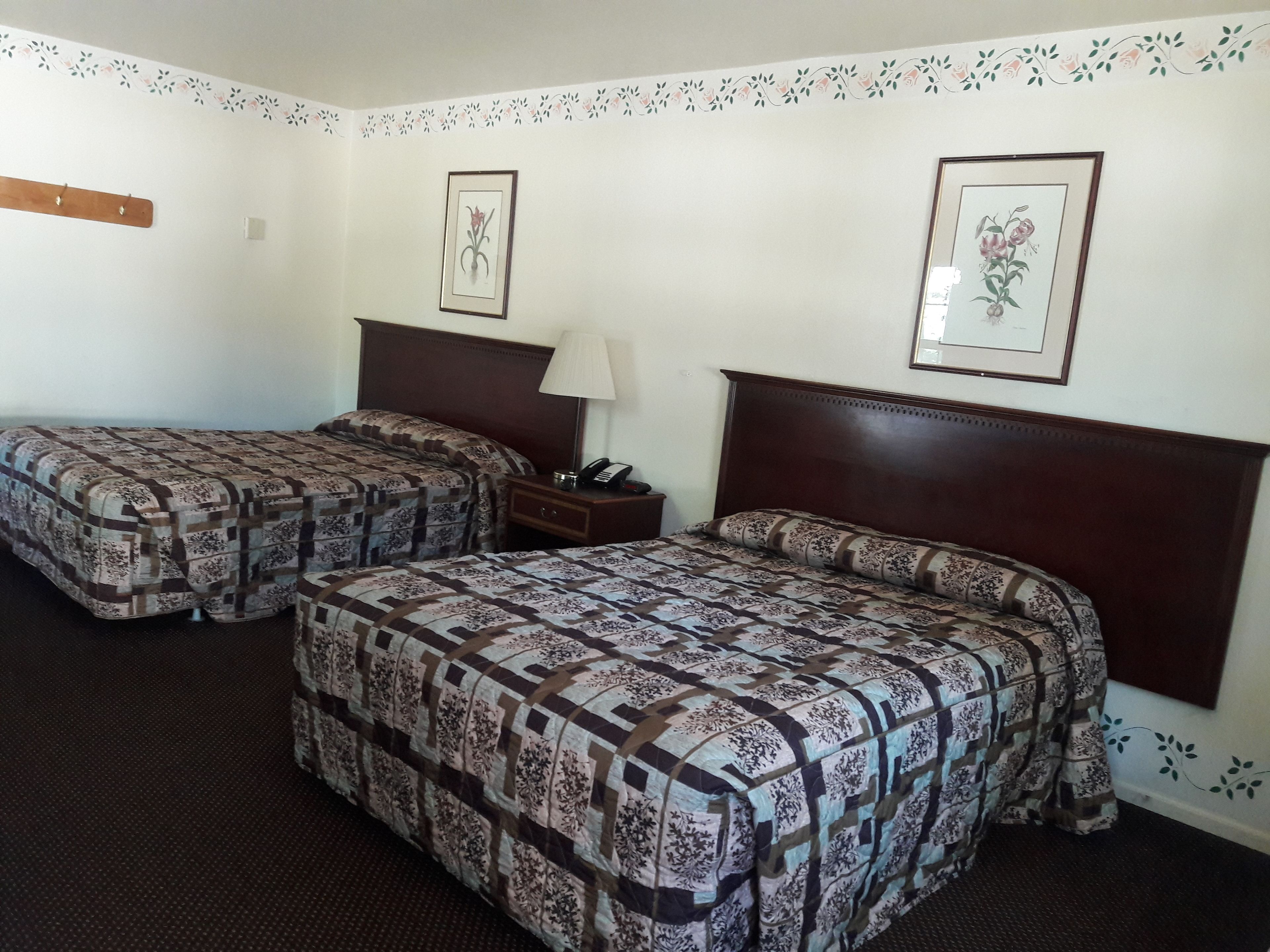 Habitació d'hotel amb dos llits, una taula de nit, una làmpada i decoracions florals a la paret.