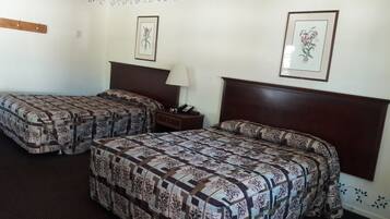 Habitación de hotel con dos camas, una mesita de noche, una lámpara y adornos florales en la pared.
