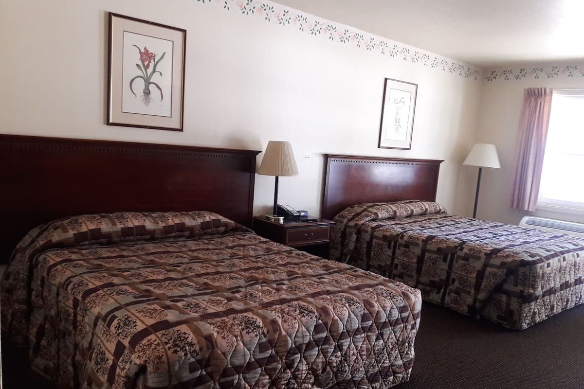 A hotel room with two beds, each with a patterned quilt, a nightstand with a lamp, and framed artwork on the walls.