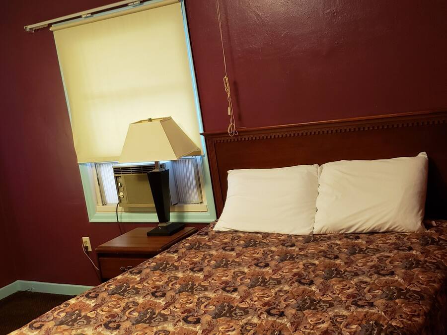 A hotel room with a bed, a nightstand, a lamp, and a window with curtains.