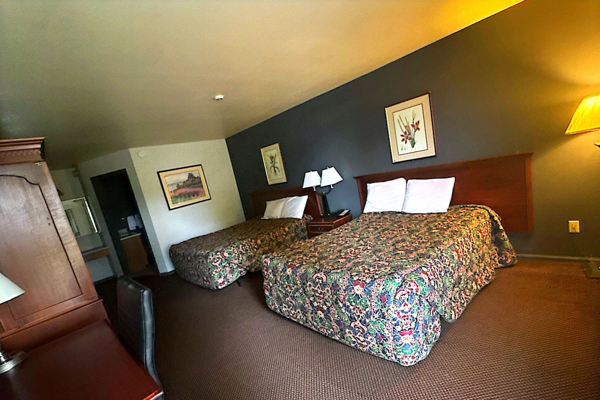 A hotel room with two beds, a wooden headboard, a desk, and a chair.