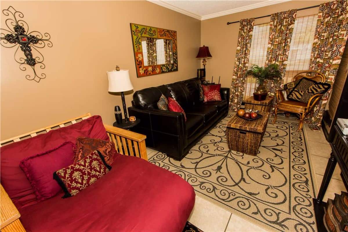 A living room with a black sofa, red and patterned cushions, a wooden coffee table, and a patterned rug.