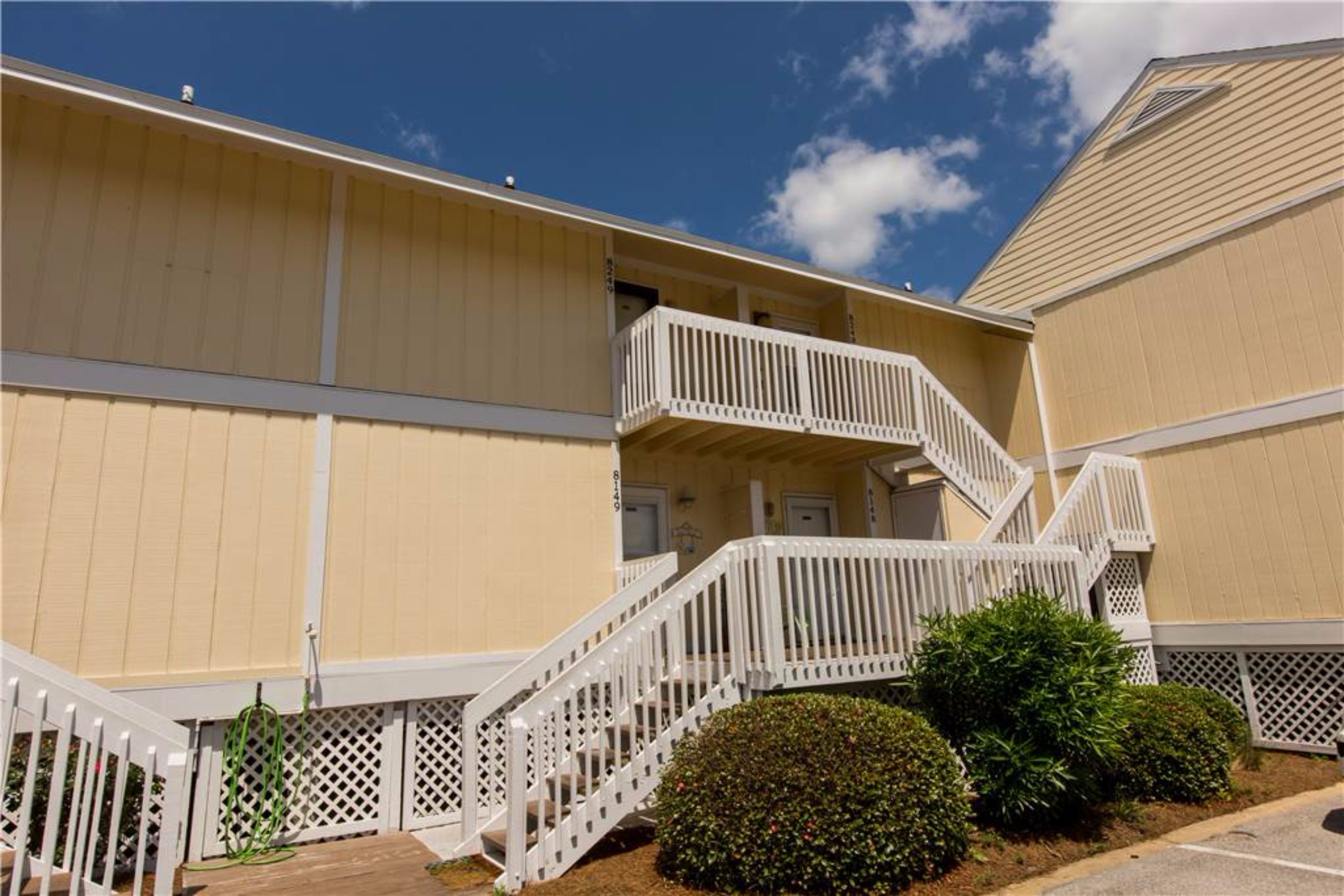A multi-story hotel with a beige exterior, white railings, and a staircase leading to the upper floors.