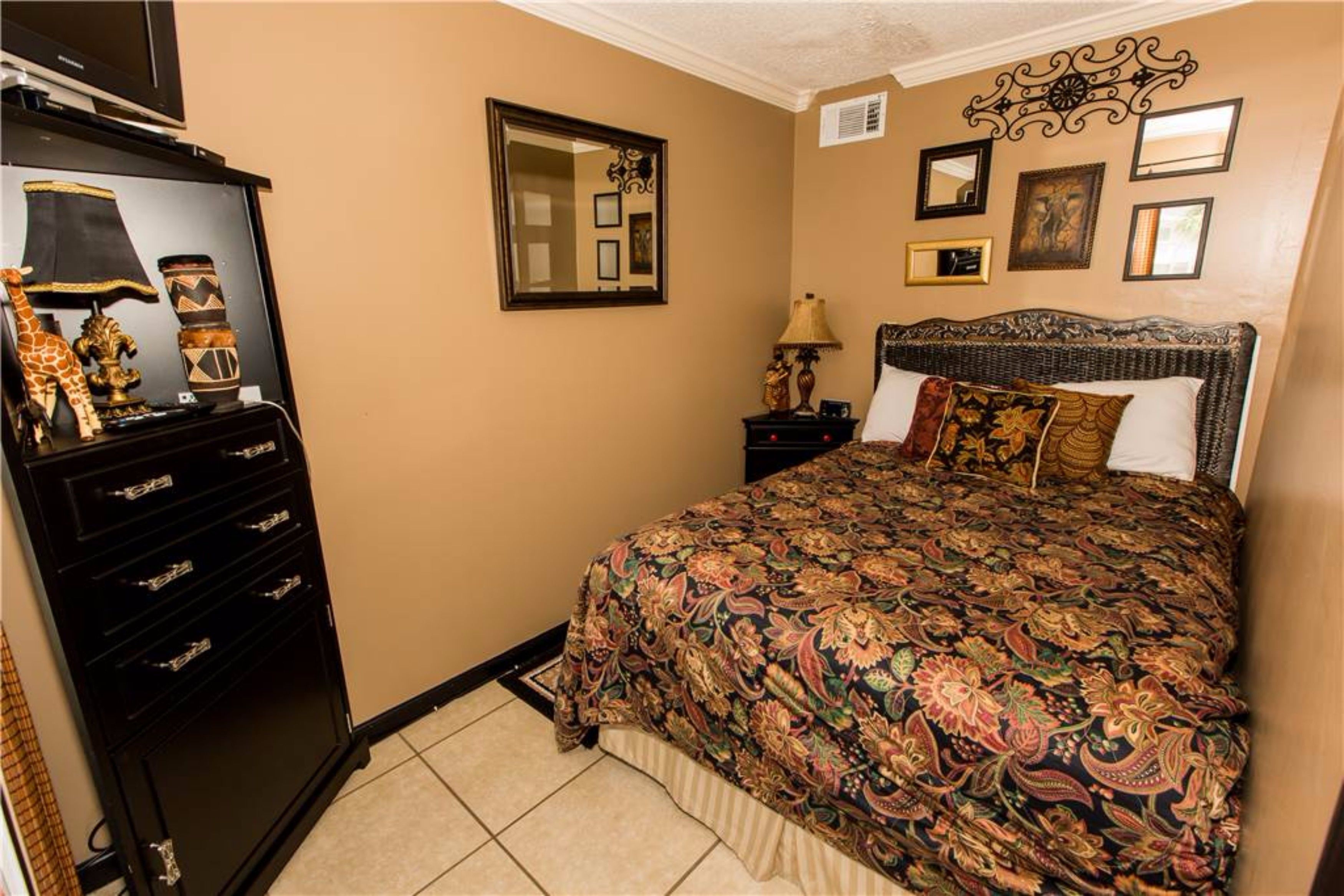 A bedroom with a large bed, a dresser, a mirror, and framed pictures on the wall.