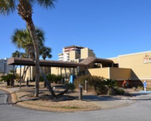 A building with a flat roof, a covered outdoor area, and palm trees. - Sandpiper Cove Studios By Holiday Isle (Destin)