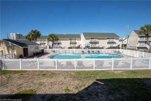 A hotel with a swimming pool surrounded by a white fence, multiple balconies, and a clear blue sky. - Sandpiper Cove Studios By Holiday Isle (Destin)