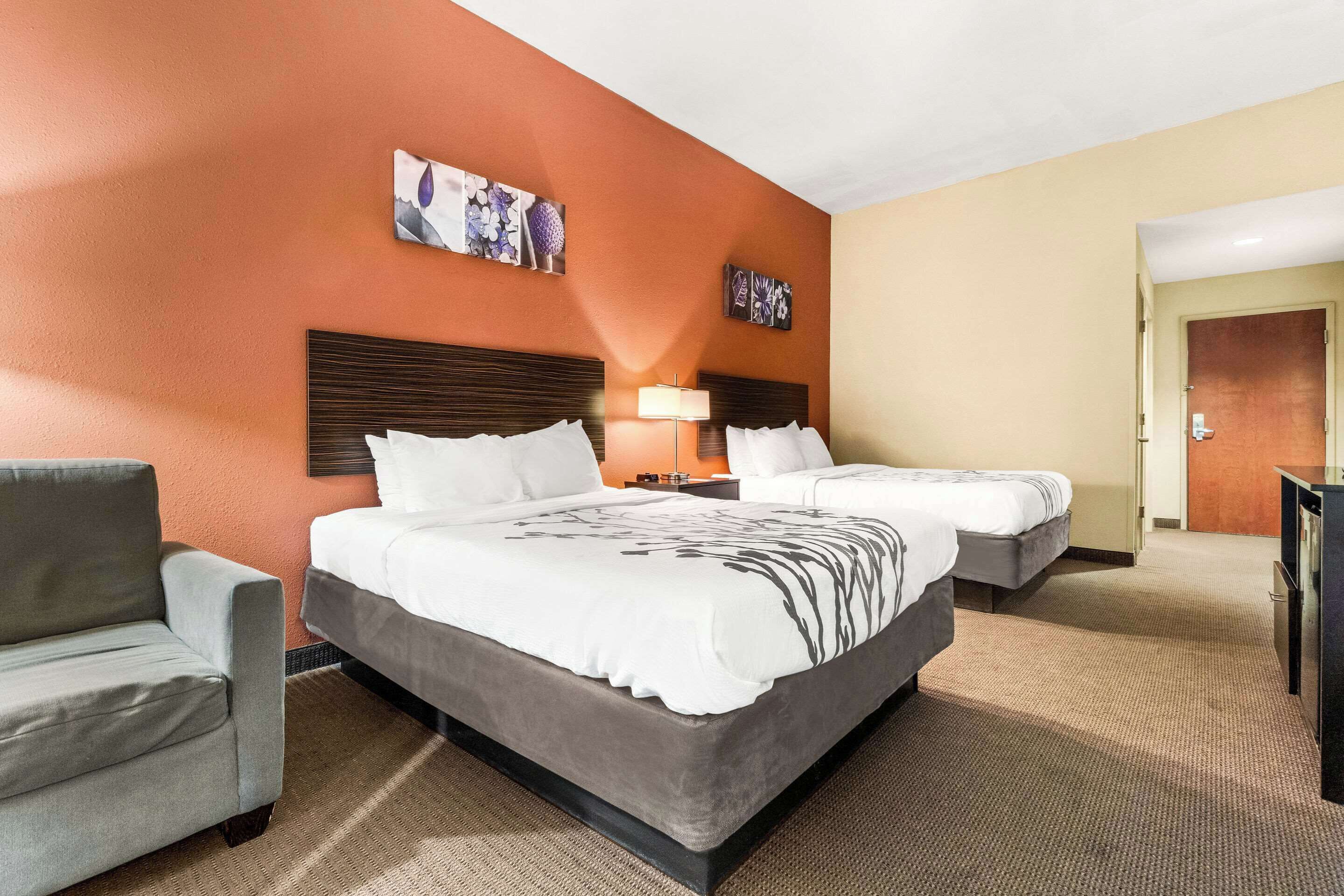 A hotel room with two beds, a sofa, a desk, and a lamp.