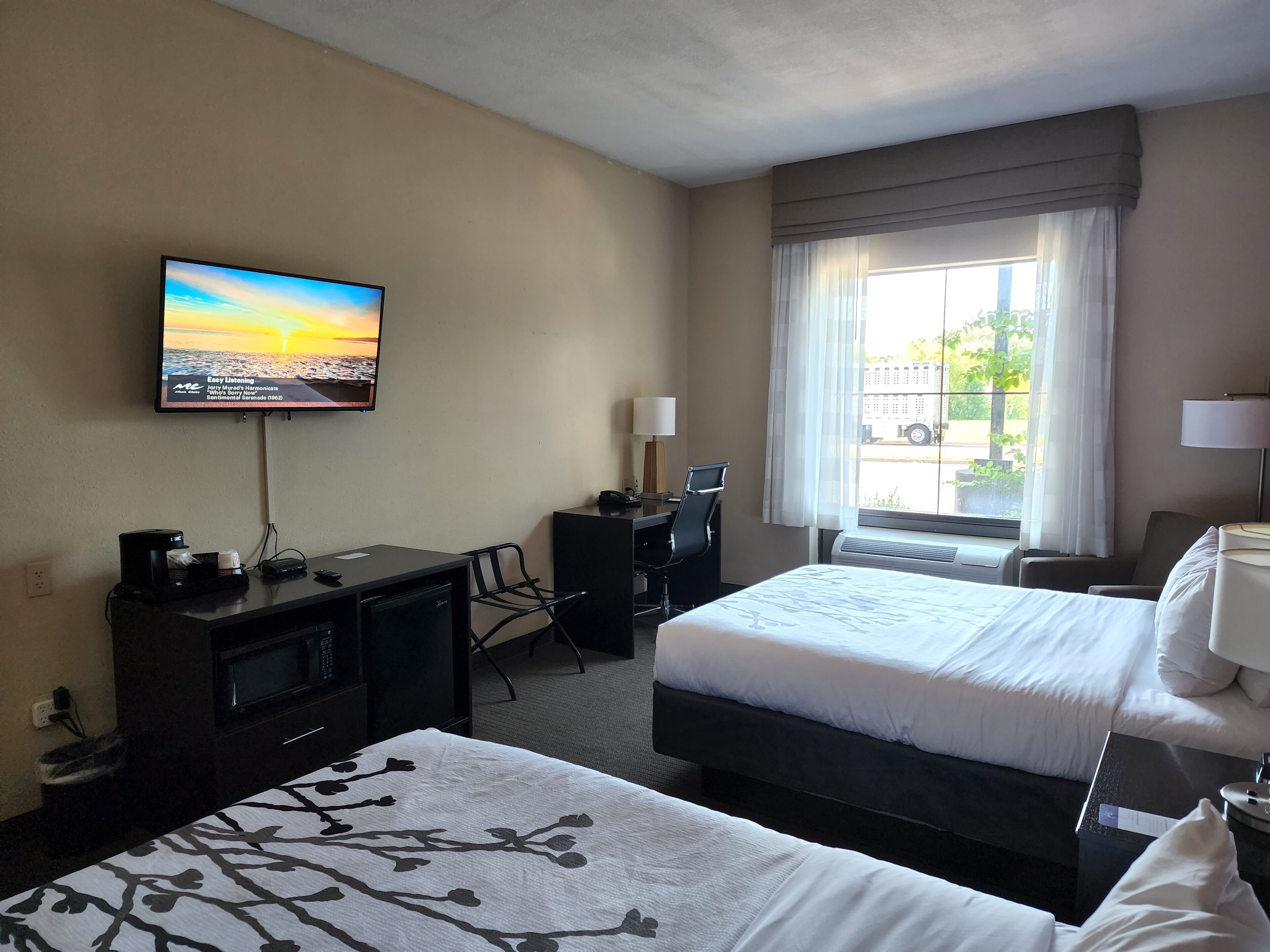 A hotel room with a bed, a desk, a TV, and a window with curtains.