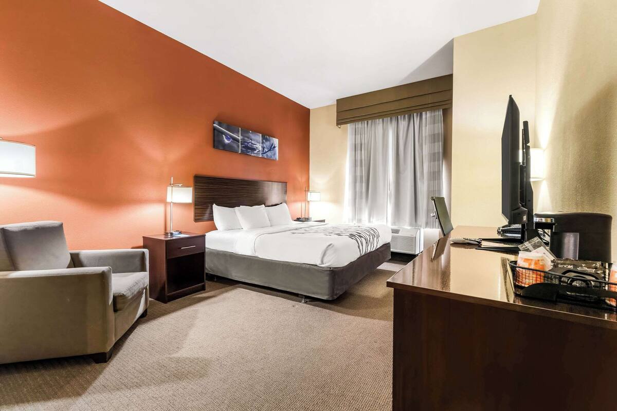 Habitación de hotel con una cama grande, un escritorio con ordenador, una silla, un televisor y una ventana con cortinas.