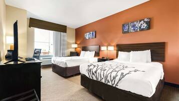 A hotel room with two beds, a desk with a computer, a TV, and artwork on the walls.