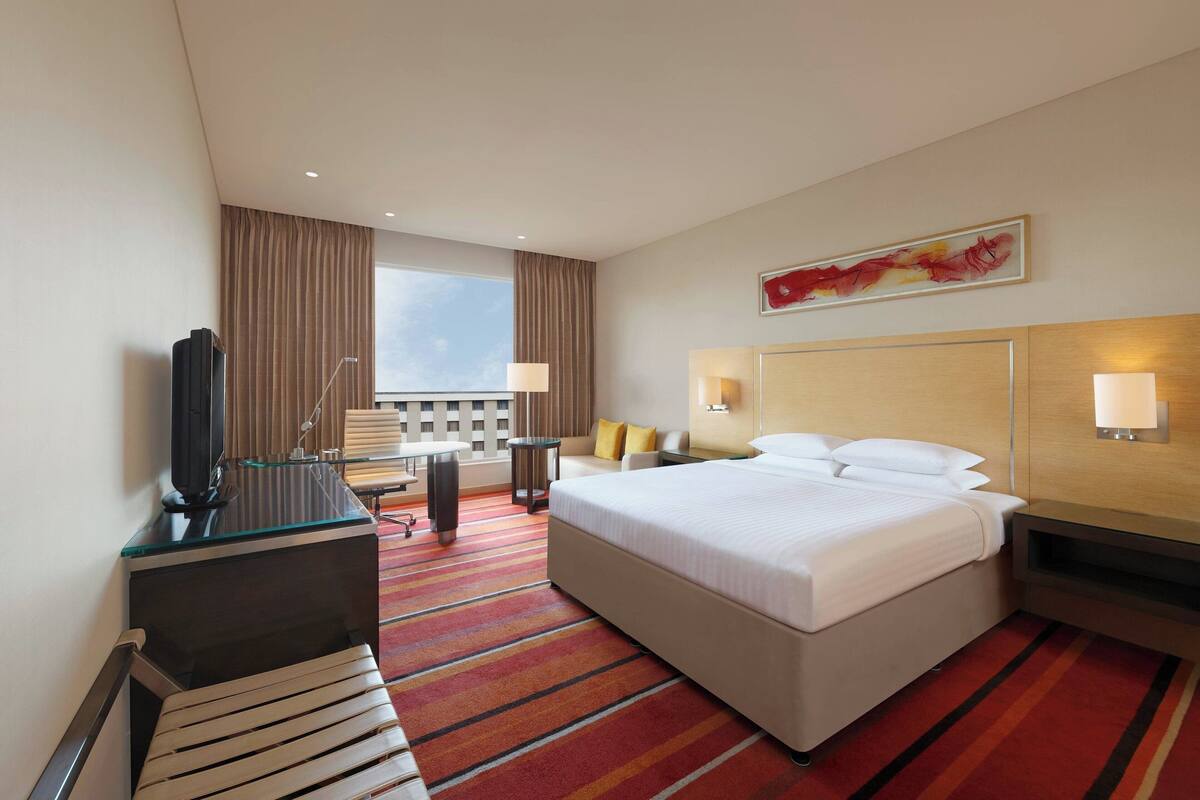 Quarto de hotel com uma cama grande, escrivaninha com computador, televisão e vista para o exterior.