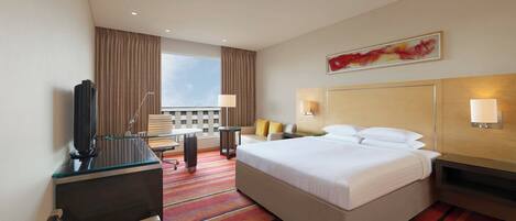Habitación de hotel con una cama grande, un escritorio con computadora, un televisor y vistas al exterior.