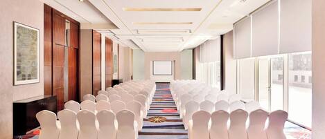 A conference room with rows of white chairs, a carpet with geometric patterns, and a large screen at the front.