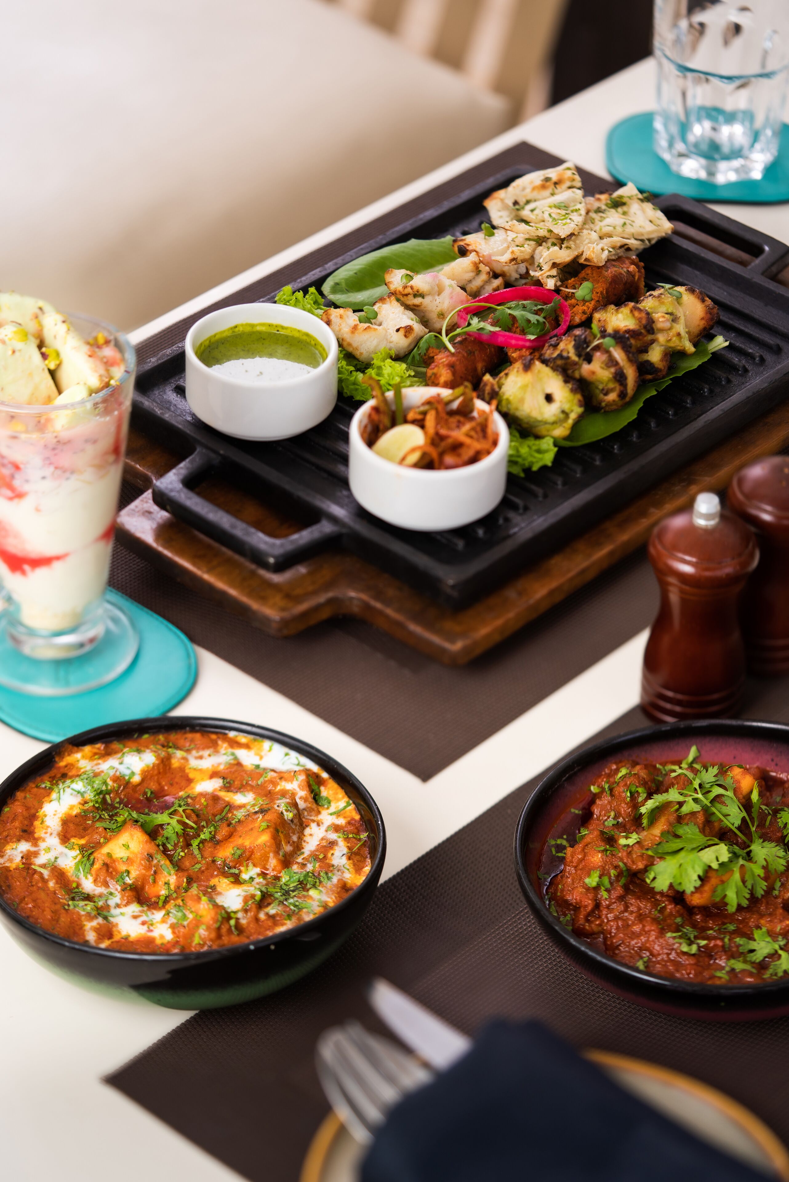 A meal with grilled chicken, vegetables, and two bowls of curry on a table.