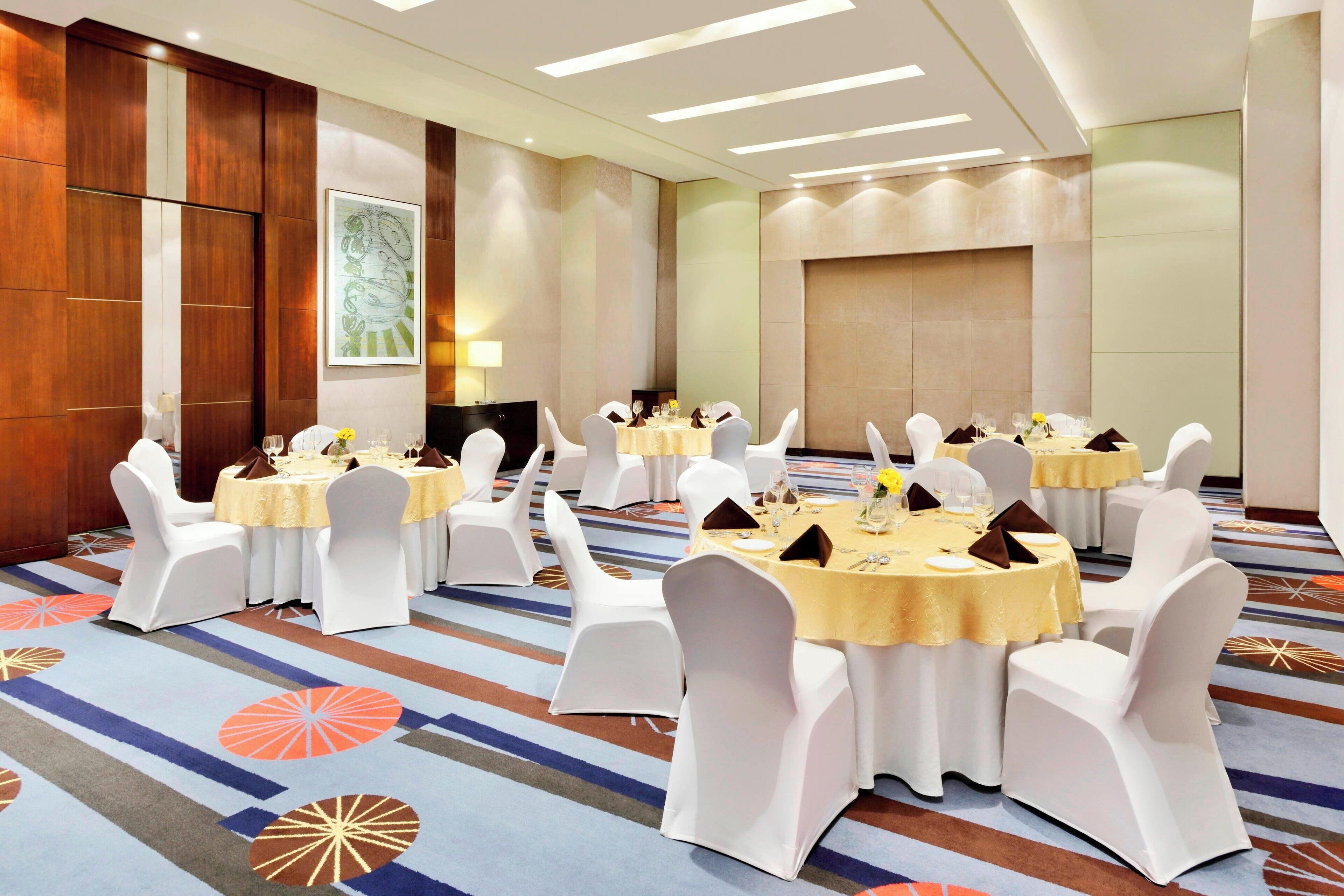 A conference room with multiple round tables, white chairs, and a carpeted floor.