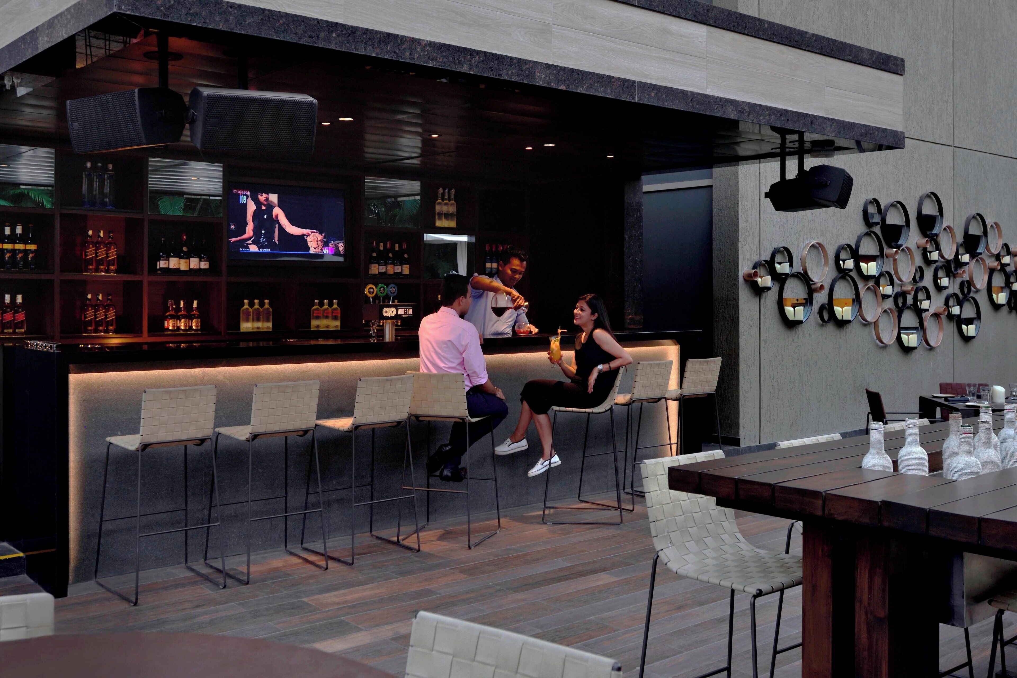 Eine moderne Bar mit einer langen Theke, Barhocker und einem Fernsehbildschirm.
