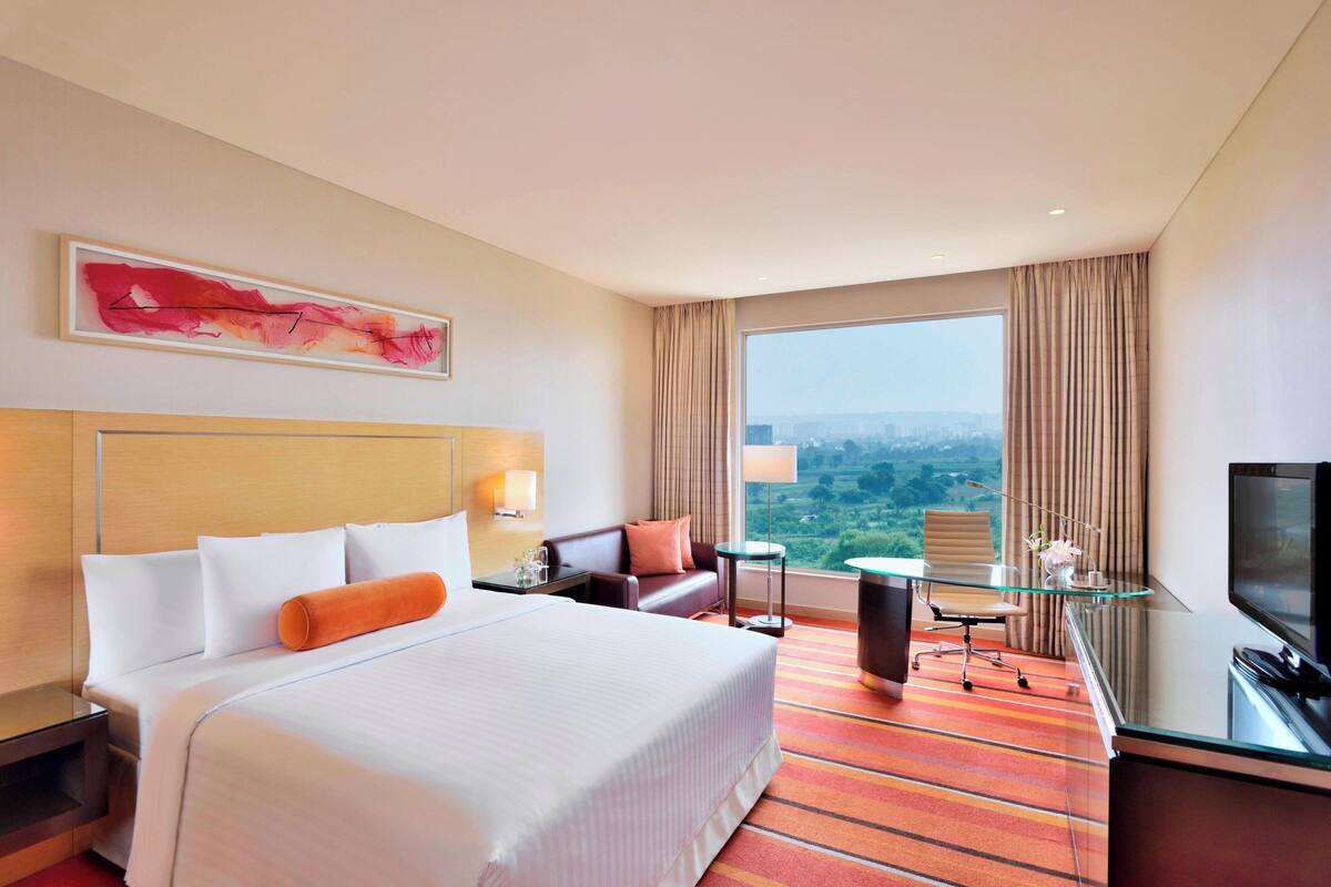 Quarto de hotel com uma cama grande, uma escrivaninha com televisão, uma mesa de vidro e vista para a cidade.
