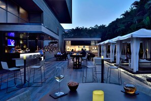 An outdoor dining area with tables and chairs, a bar, and a seating area with umbrellas. - Courtyard by Marriott Pune Hinjewadi (Paud)