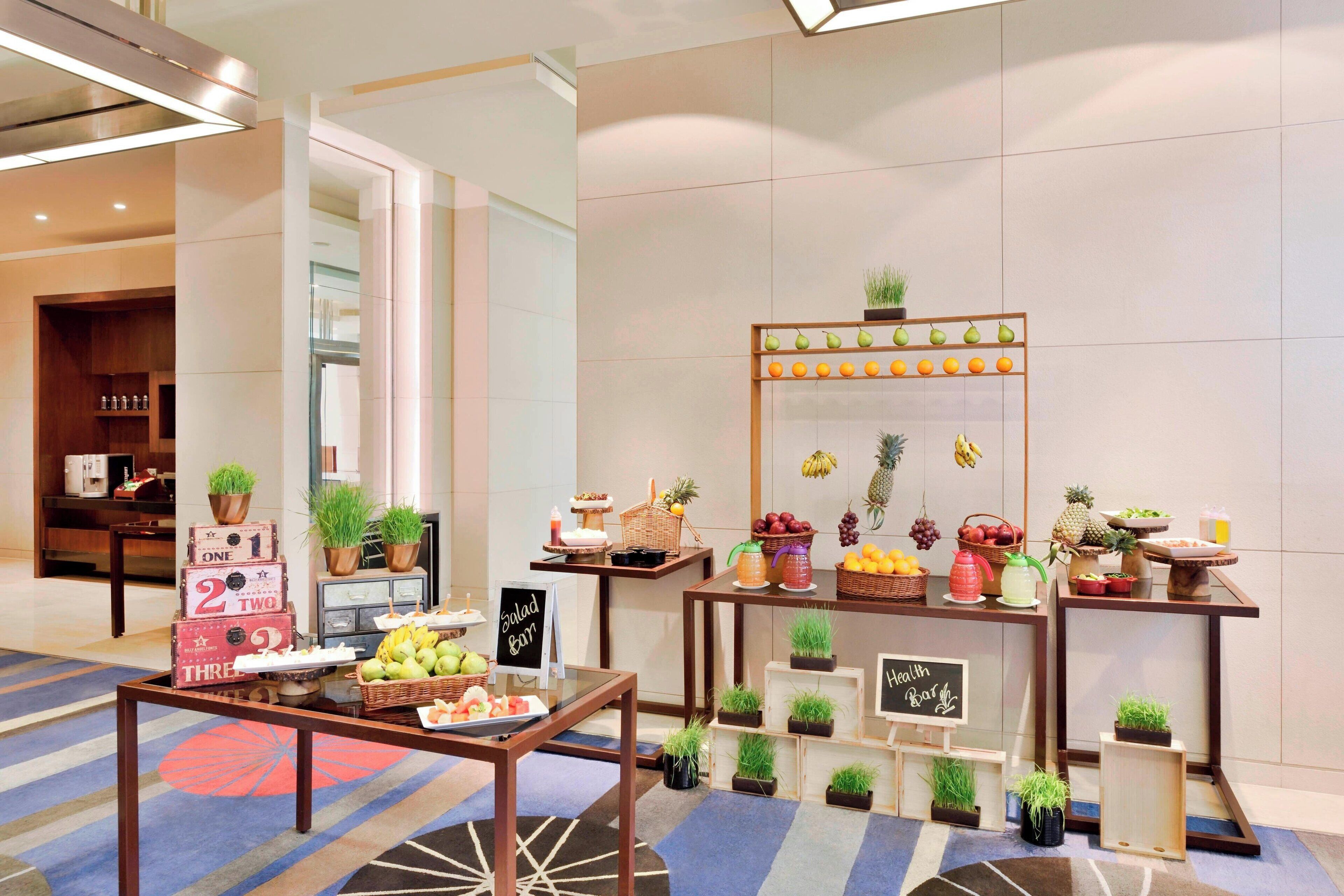 A hotel lobby with a fruit and salad bar, wooden tables, and potted plants.