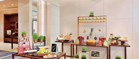 A hotel lobby with a fruit and salad bar, wooden tables, and potted plants.