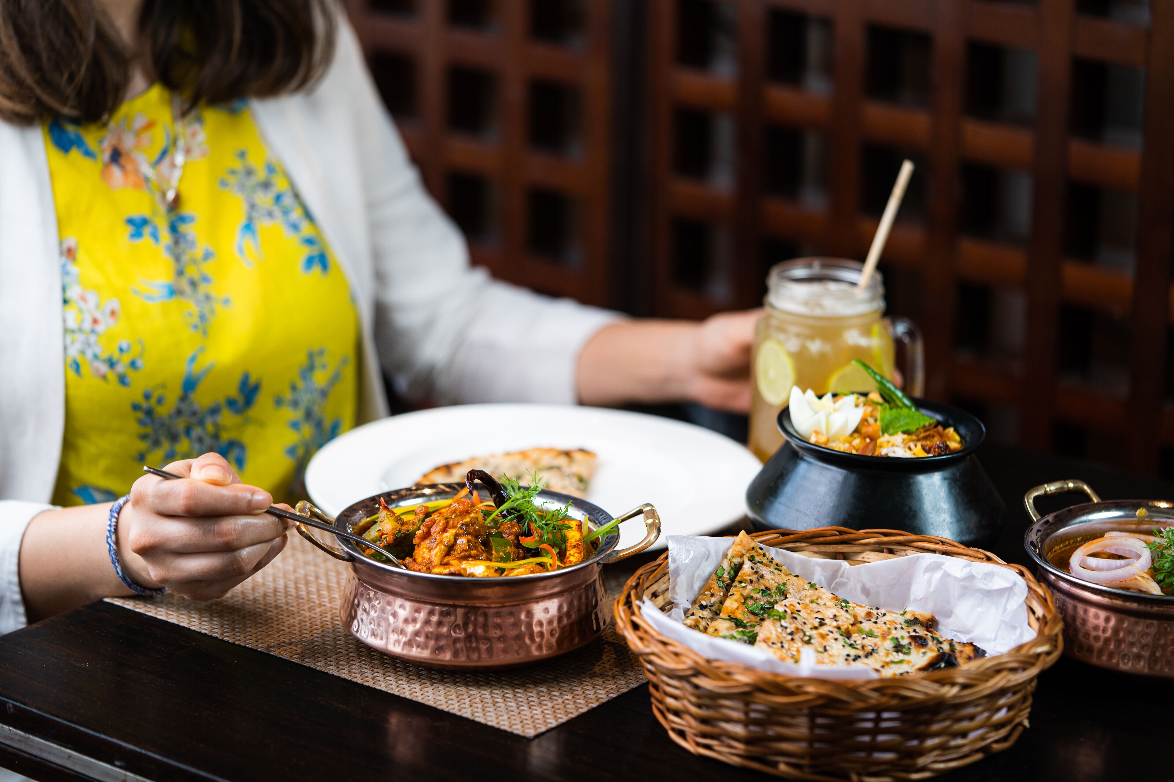 A dining table with a meal, including a bowl of food, a basket of bread, and a jar of sauce.