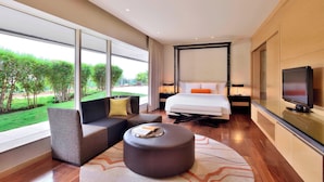 Una habitación de hotel moderna con una cama grande, un sofá, un otoman redonda y un televisor.