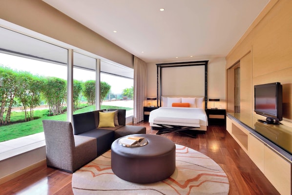 Una habitación de hotel moderna con una cama grande, un sofá, un otoman redonda y un televisor.