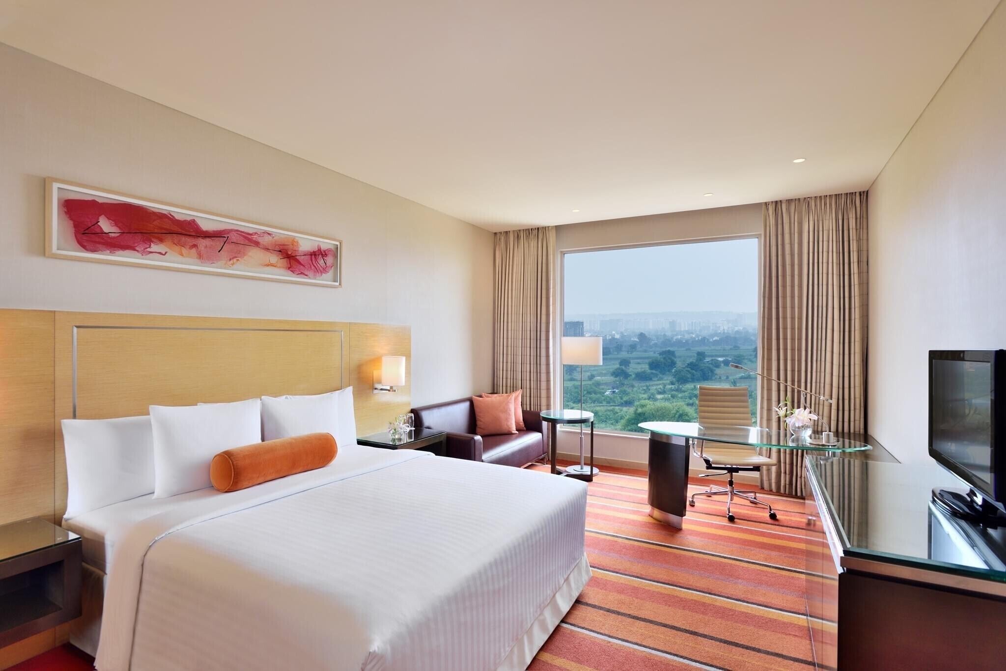Habitación de hotel con una cama grande, un escritorio con silla, televisión y vistas a la ciudad.
