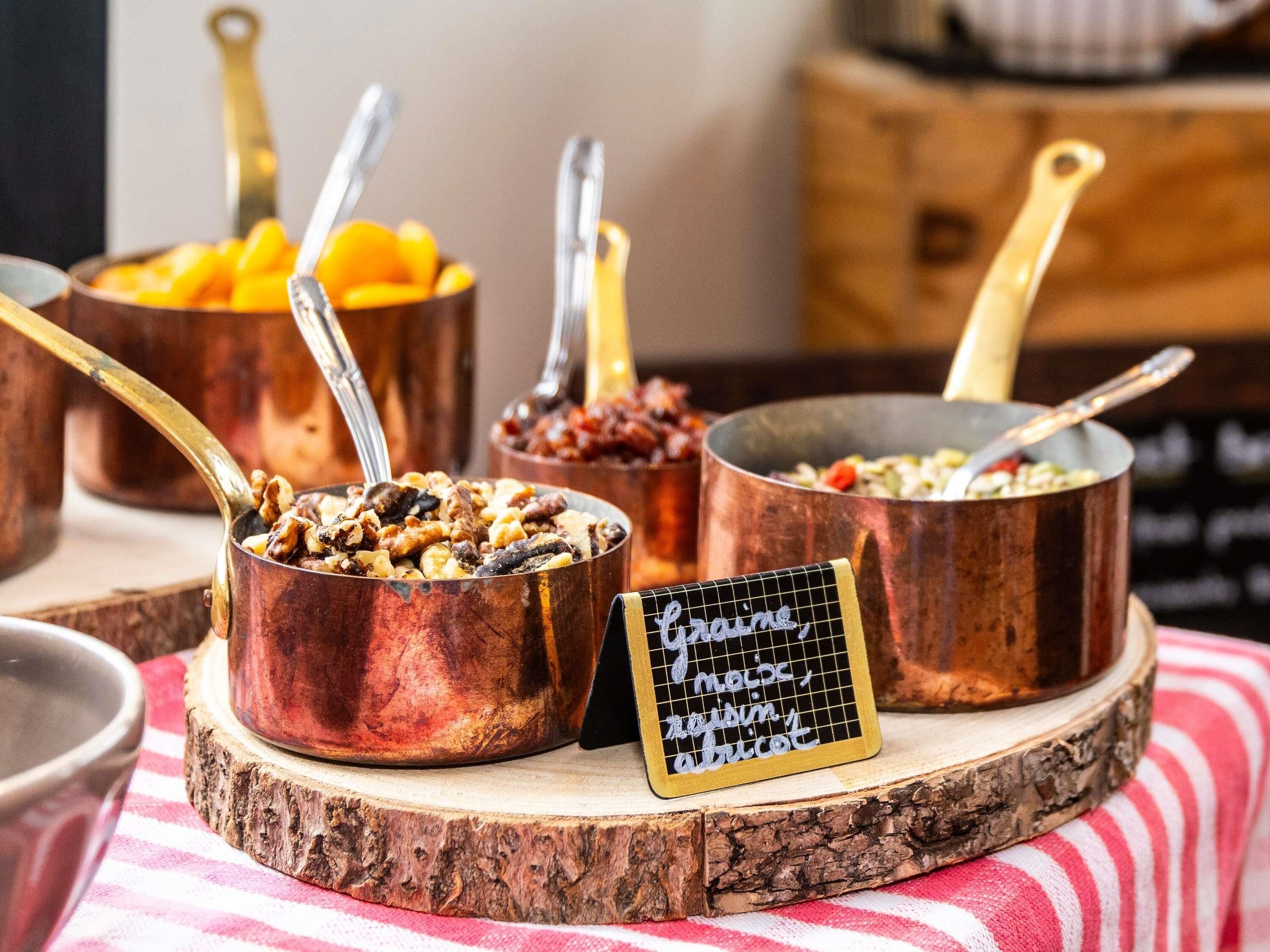 Une présentation de plats variés dans des récipients en cuivre, avec une pancarte indiquant : « Céréales, noix, graines et fruits secs ».