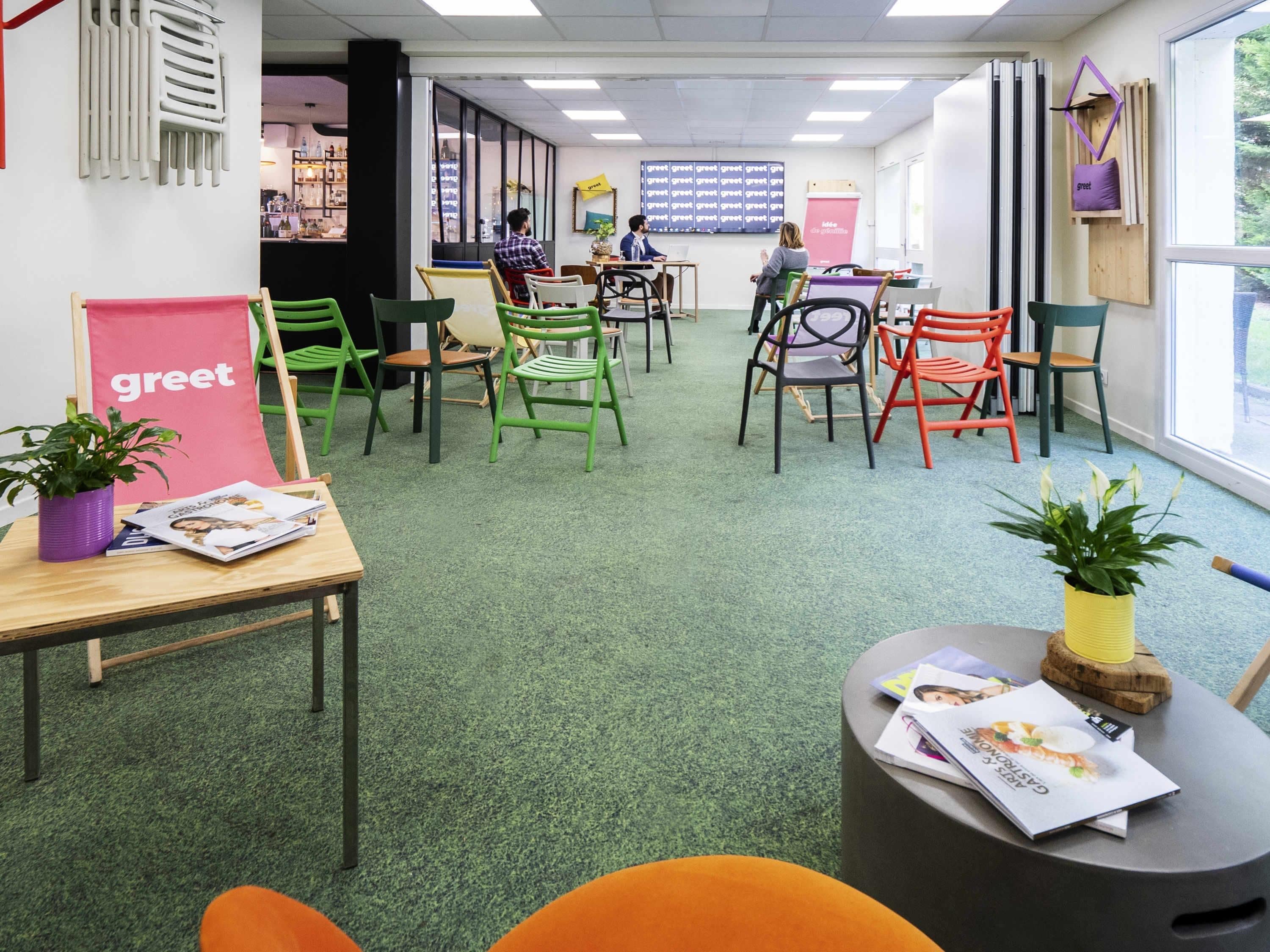 Een modern interieur met groen tapijt, meerdere zithoeken en uitzicht door grote ramen.