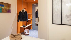 Een hotelkamer met een bed, een kapstok, een deur naar een andere kamer en een lijst aan de muur.