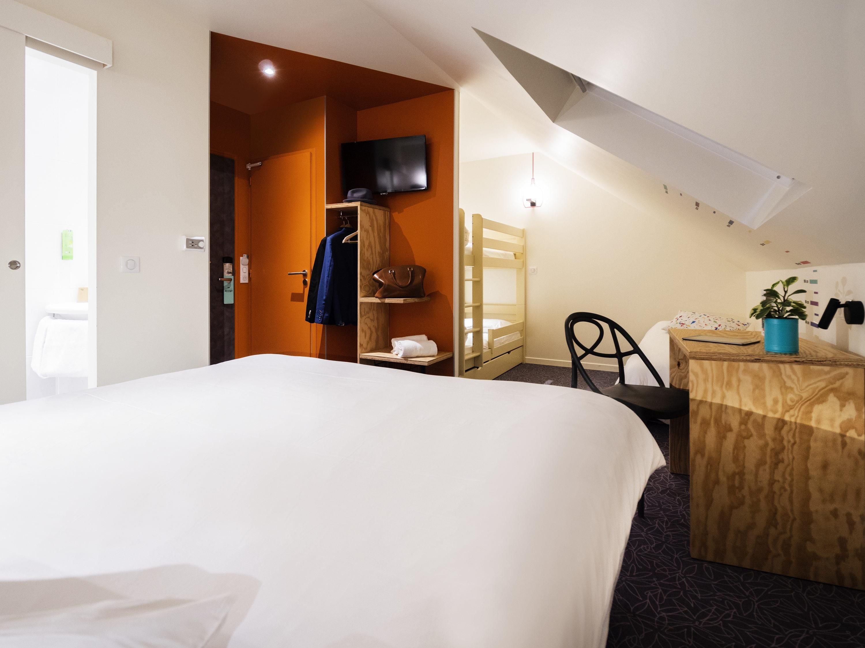 Una habitación de hotel con cama, escritorio, silla, televisor y armario.