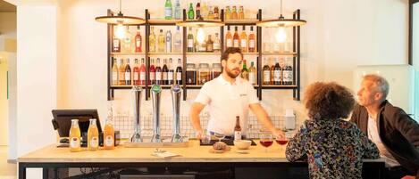 A bar area with a bartender, stools, a counter with bottles, and a shelf with various bottles.
