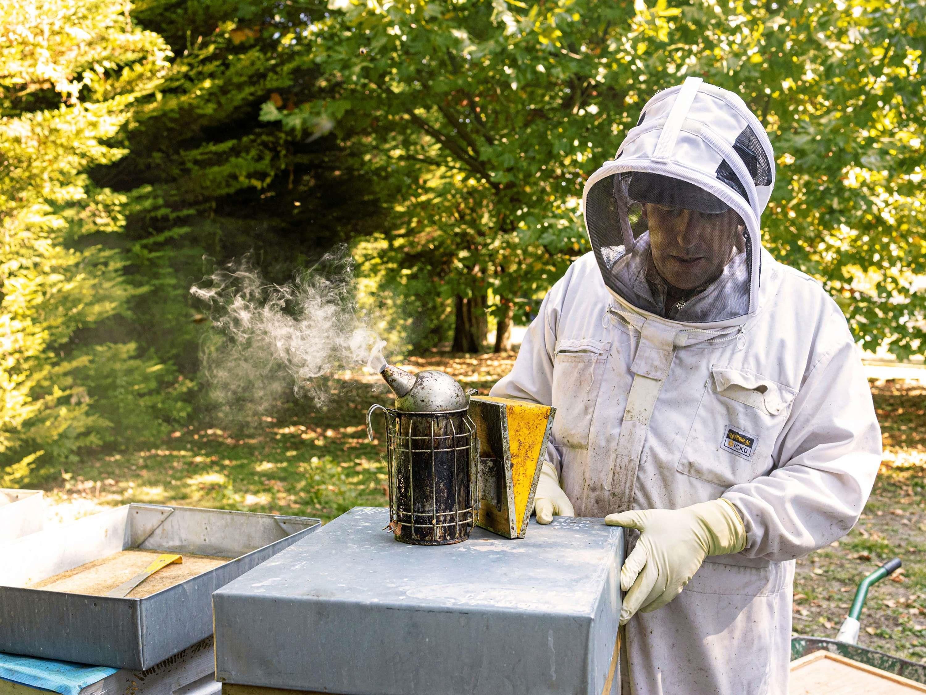 A person in protective gear working with a smoking apparatus outdoors.