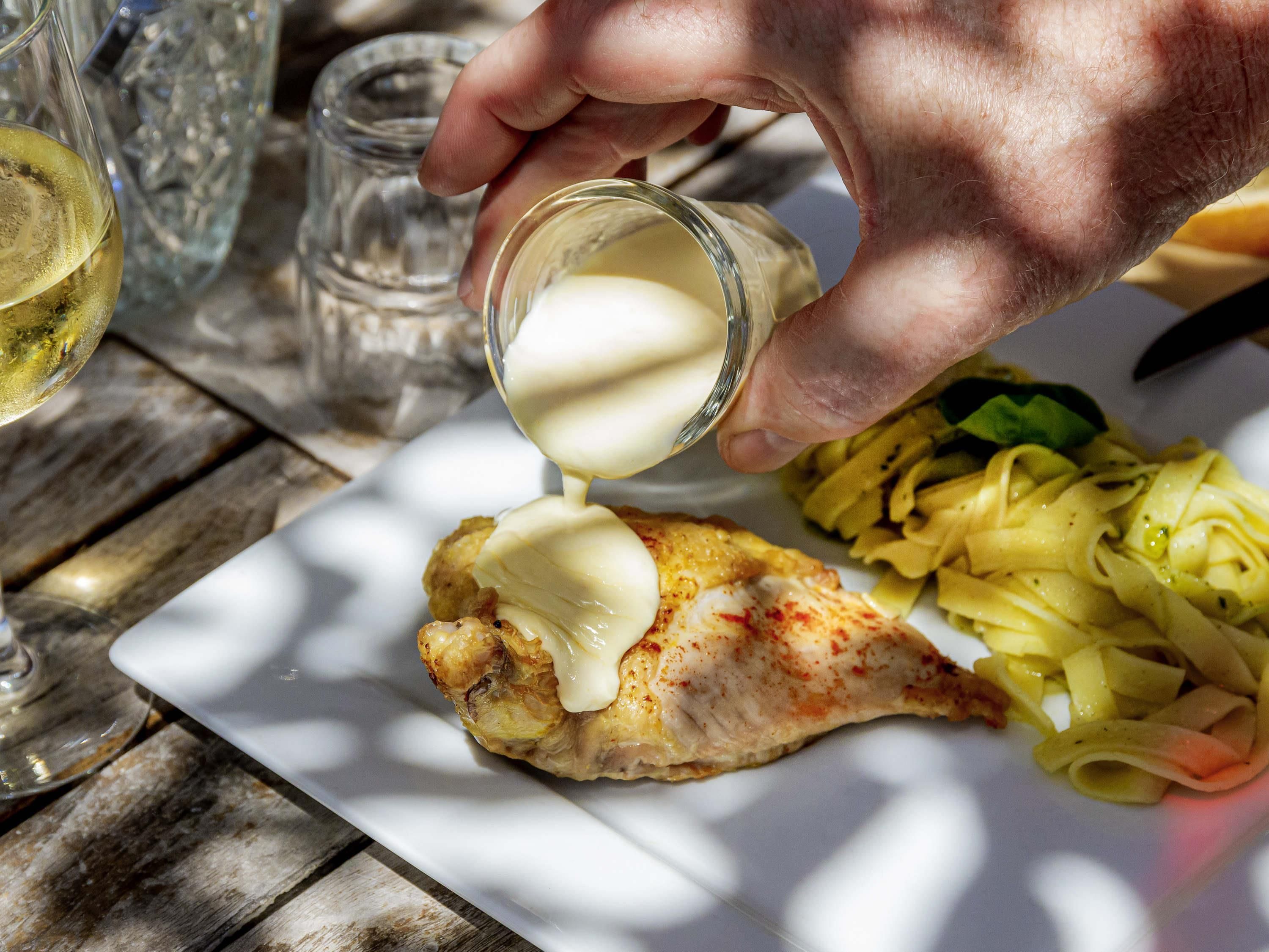 Une main verse de la sauce sur un morceau de poulet dans une assiette.