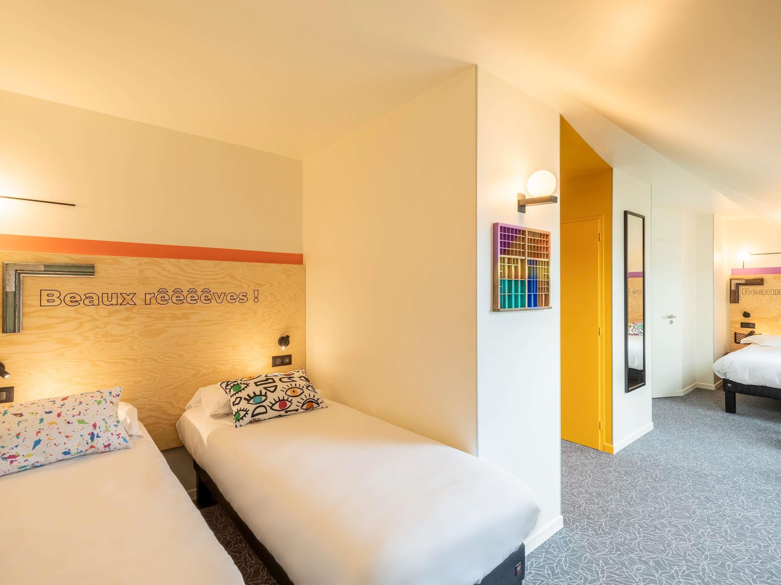 Habitación de hotel con dos camas, cabecero de madera, una obra de arte colgada en la pared y una puerta que da a otra habitación.