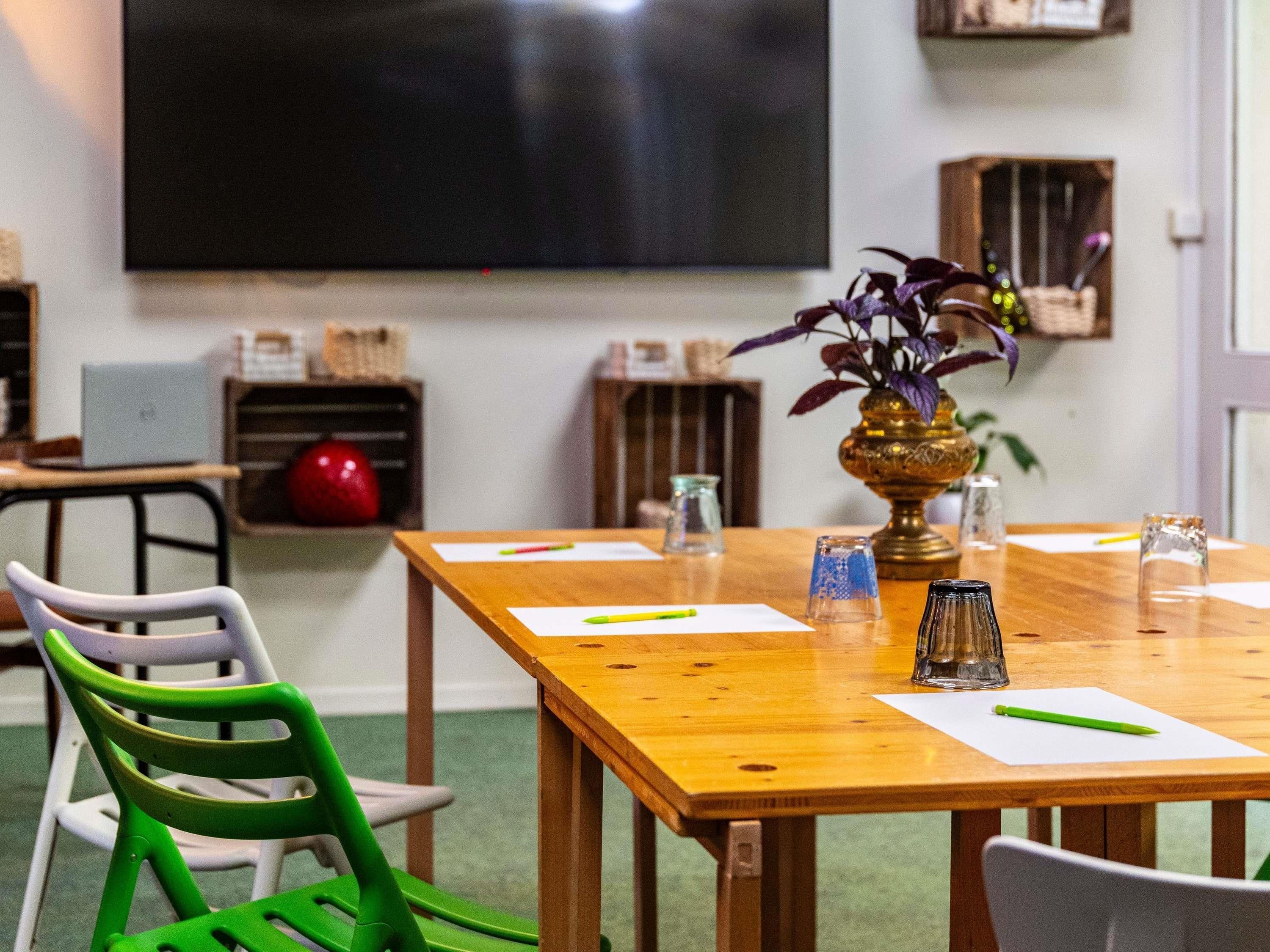 A conference room with a wooden table, chairs, a projector screen, and a plant.