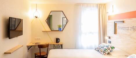 A hotel room with two beds, a desk with a chair, a TV mounted on the wall, a mirror, and a window with curtains.
