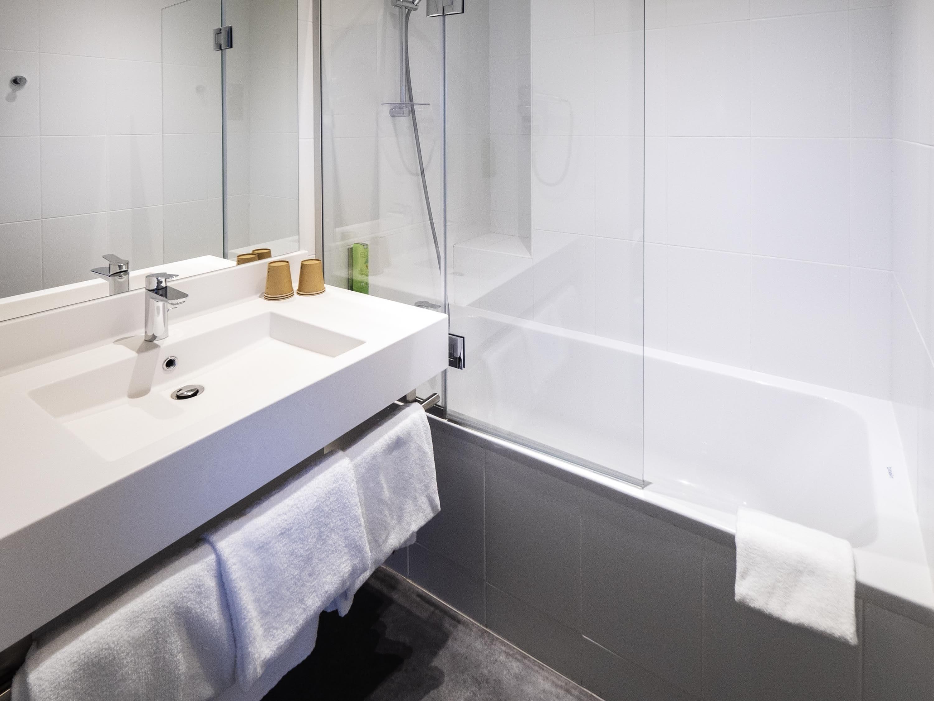Un baño moderno con lavamanos blanco, espejo y cabina de ducha de vidrio.
