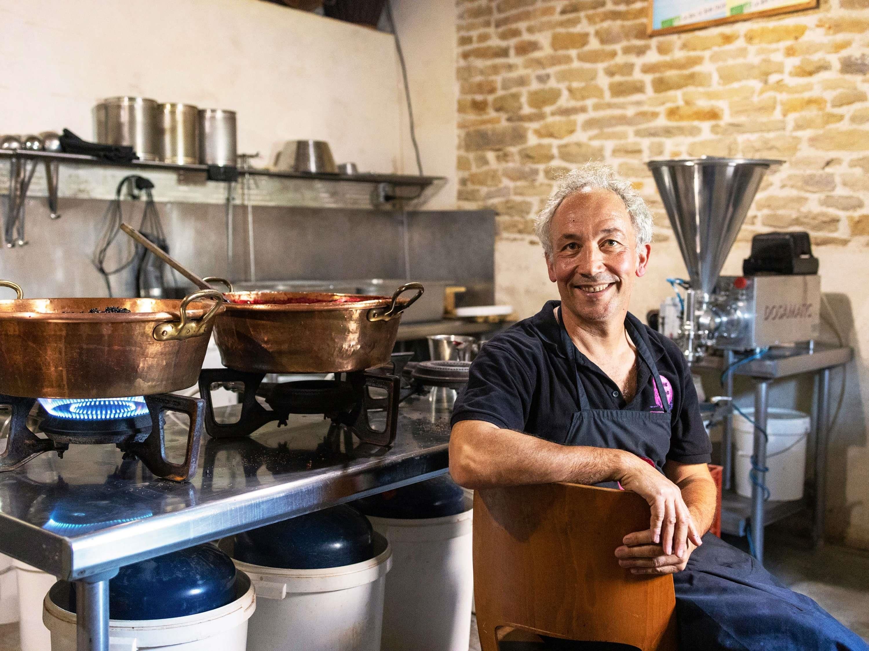 A kitchen with copper pots on a stove, a person in a dark apron, and a stone wall in the background.